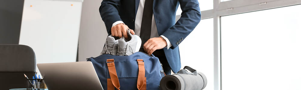 Young businessman in a suit putting his running shoes into his gym bag